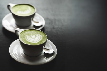 59153510 - two cups of matcha latte with latte art on black table. top view.
